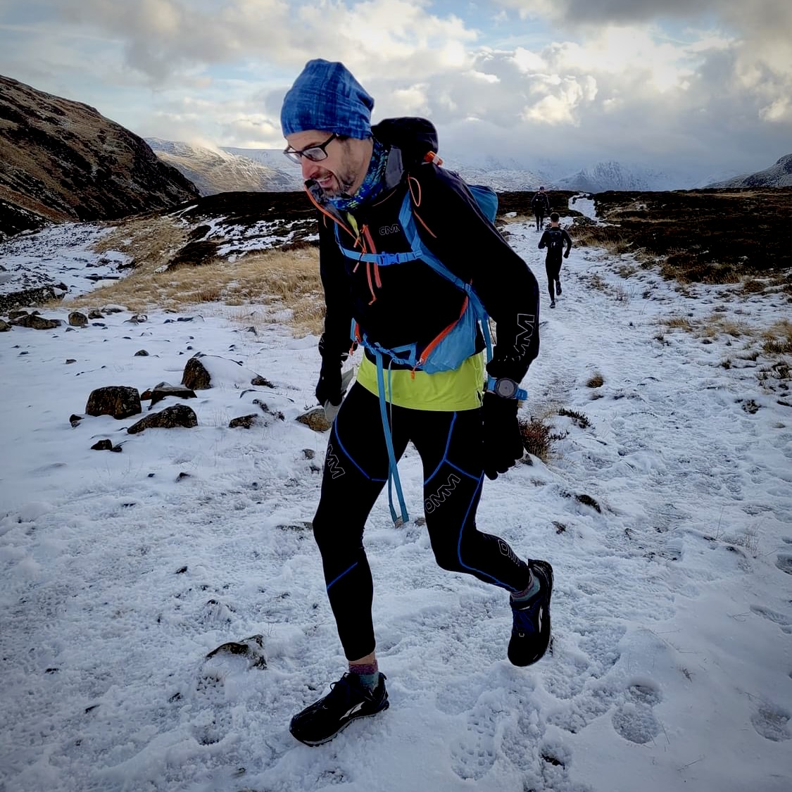 Runner with backpack in the mountains with heavily trodden snow on the ground.