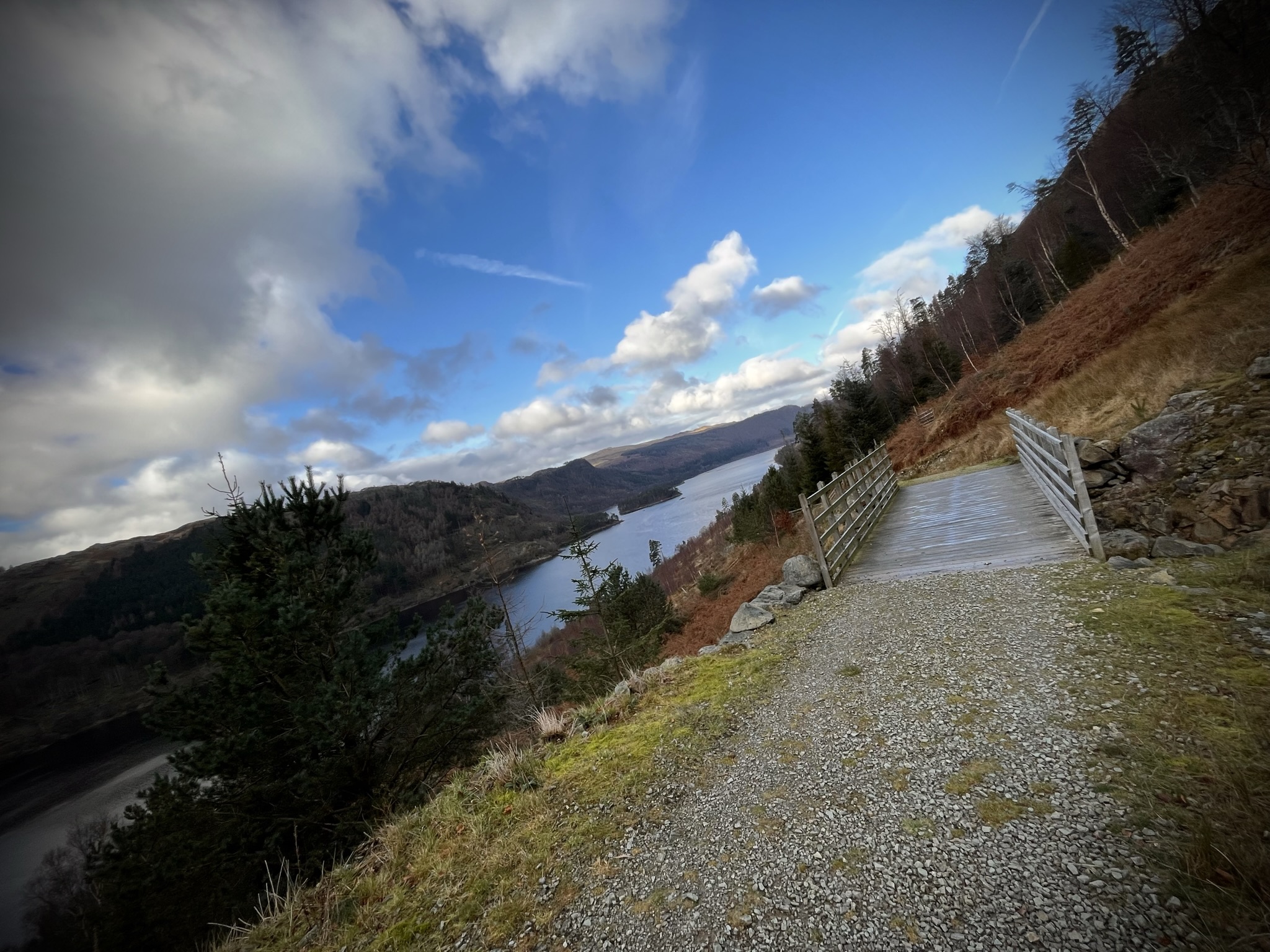 A forestry road with a wooden bridge in the foreground with Thirlmere in the background.