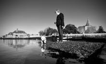 A lady and her dog stand at the waters edge.