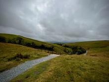 A path disappears down a hill with grey clouds in the sky.